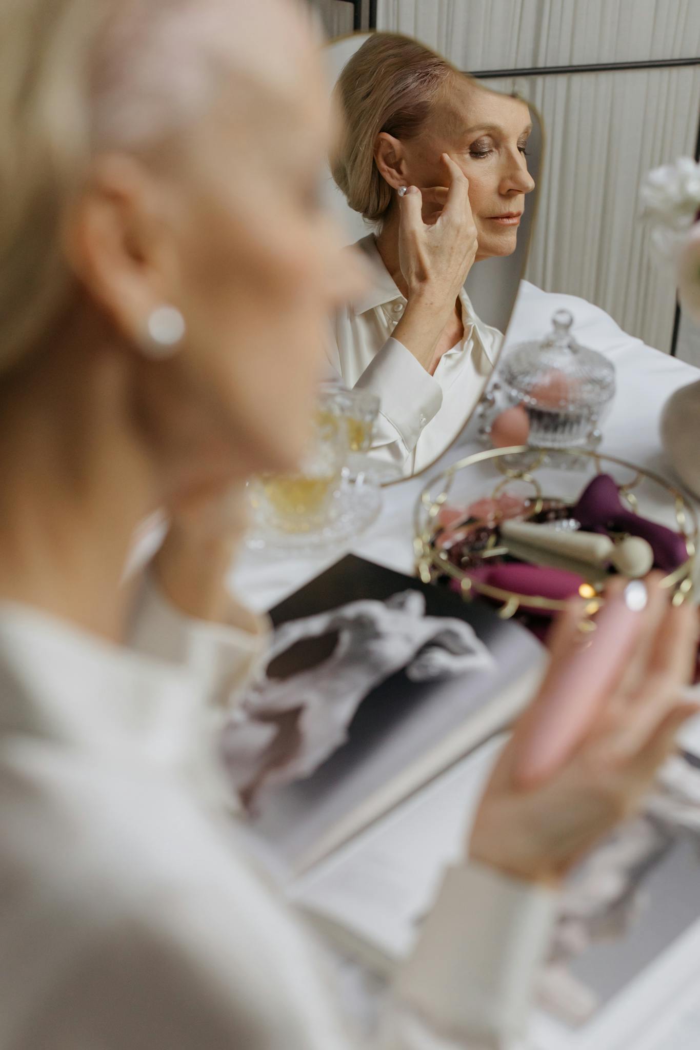 Senior woman applying makeup in front of a mirror, showcasing elegant beauty and reflection.
