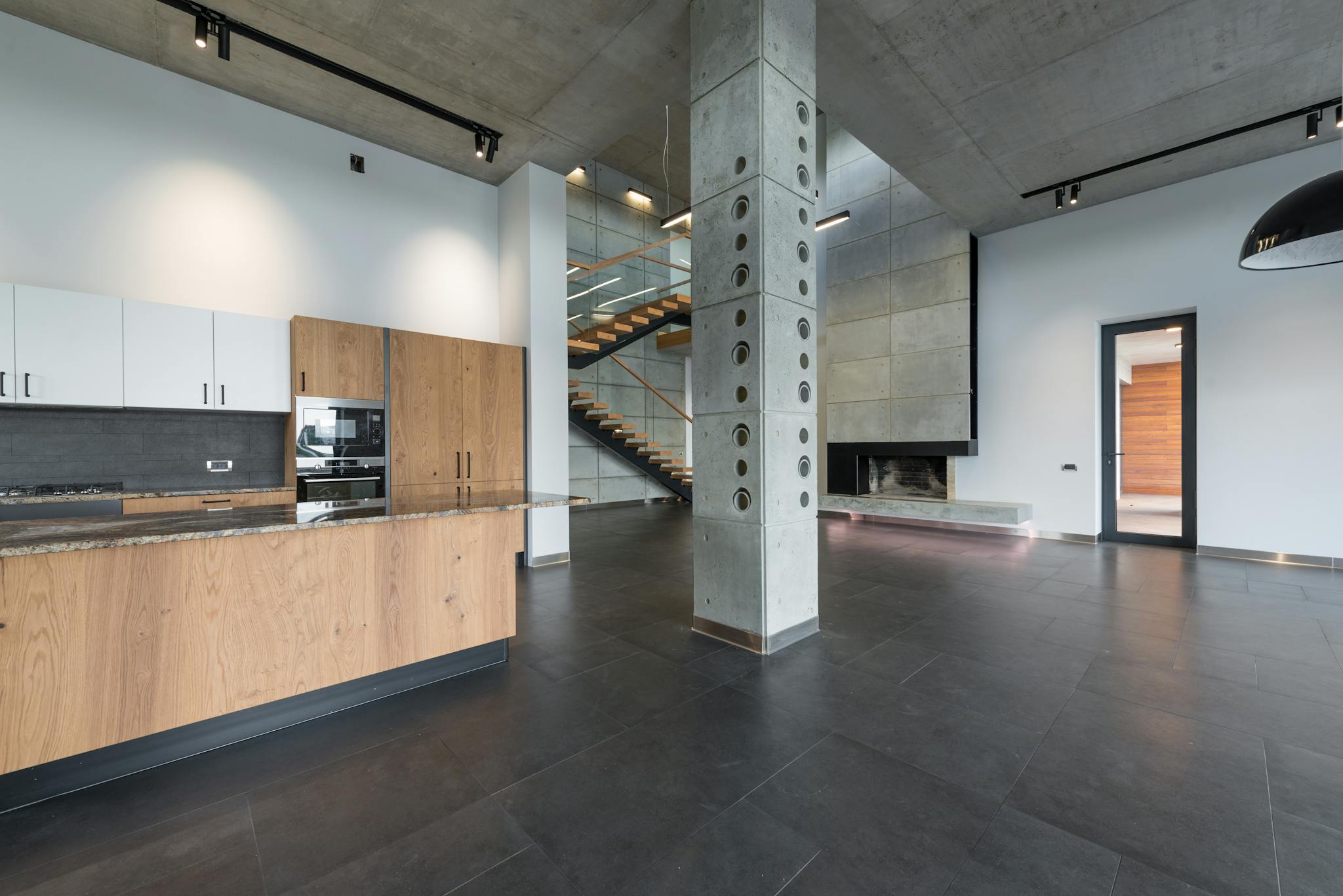 Spacious lobby with marching stairs and wooden kitchen furniture in corner near column