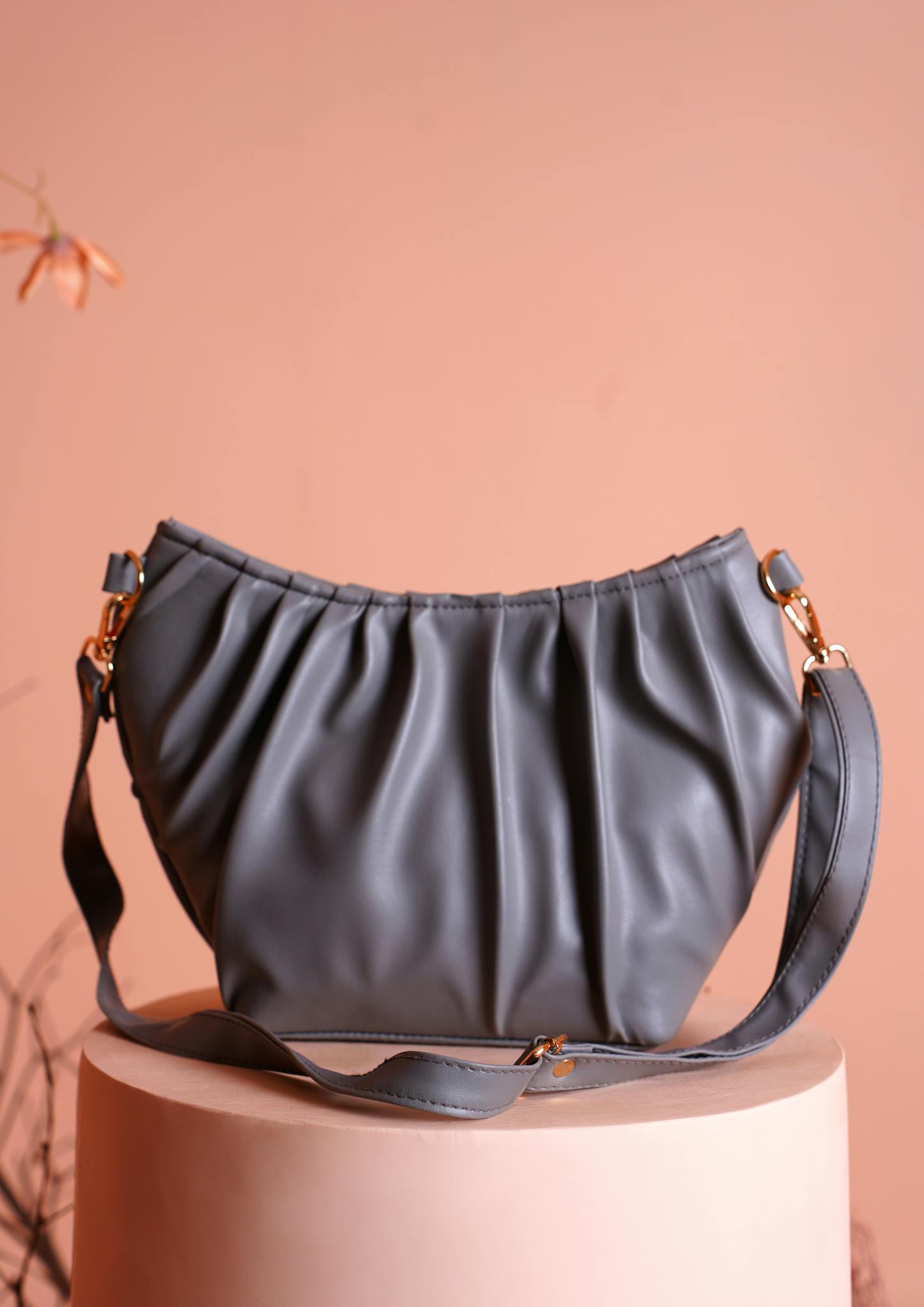 Stylish gray leather handbag with a ruched design on a sleek pedestal, perfect for fashion use.